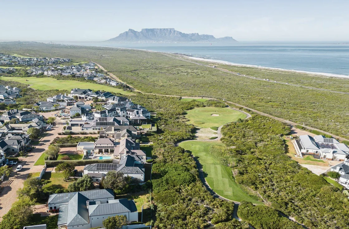 Aerial view of a golf estate on the Atlantic coast, with Table Mountain in the distance.